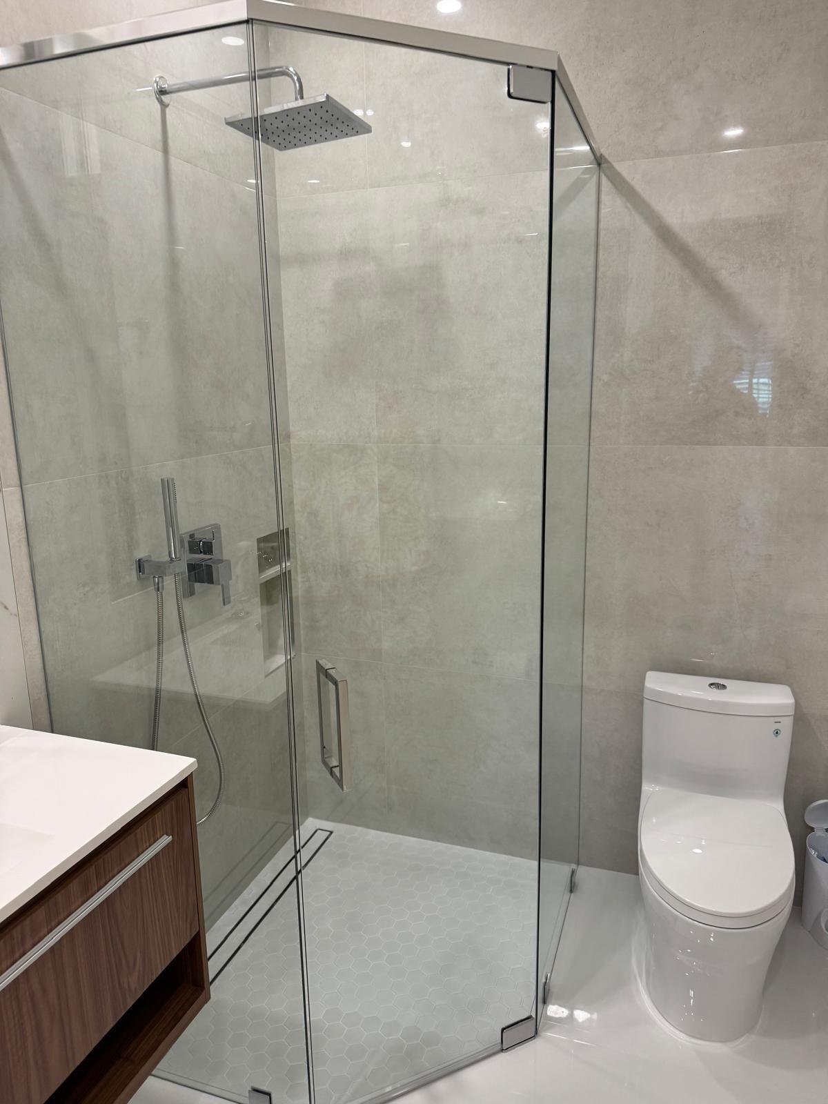 Frameless glass shower enclosure beside a floating walnut vanity