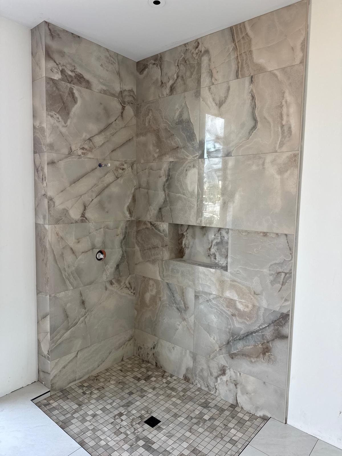 Natural stone shower enclosure with a recessed niche and mosaic floor