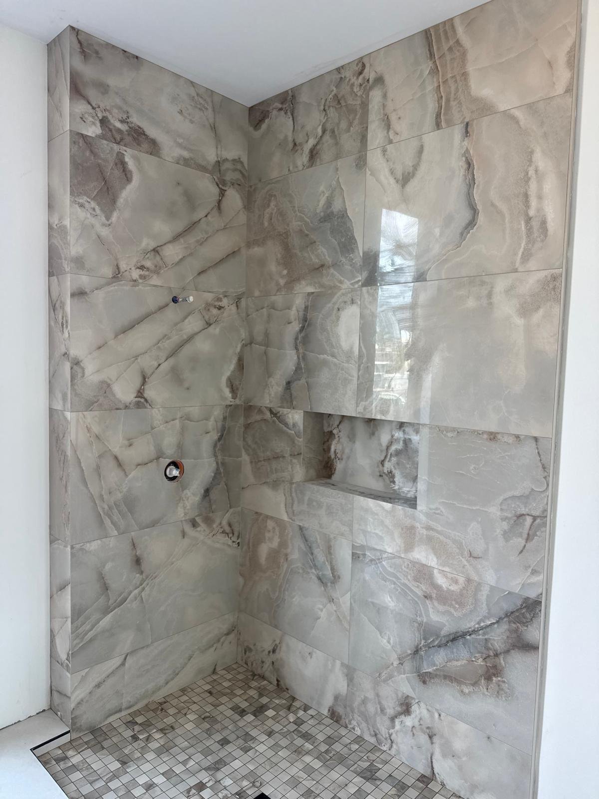 Full-height natural stone shower walls above a mosaic tile shower floor
