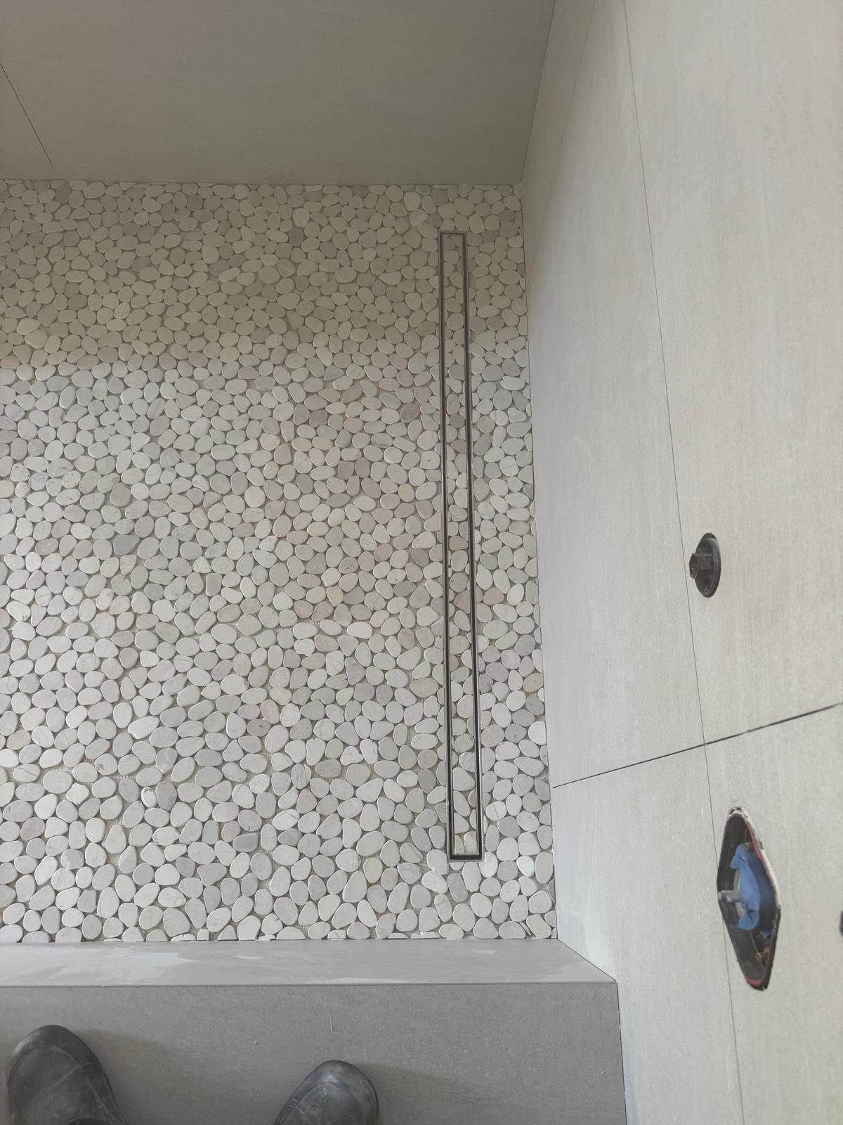 Built-in shower bench with pebble mosaic floor and linear drain